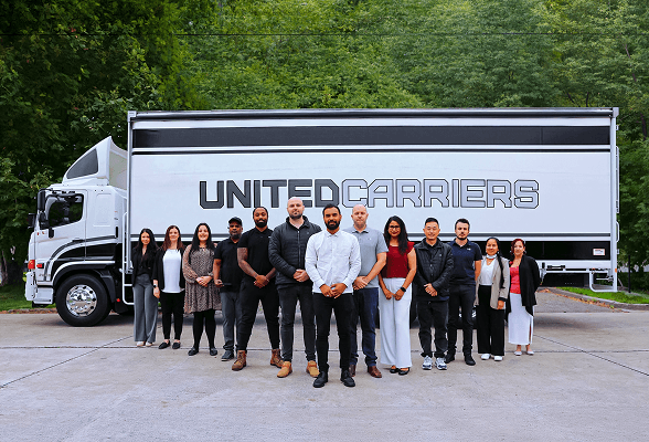 Group of twelve diverse people standing in front of a ENG Gümrük truck outdoors.